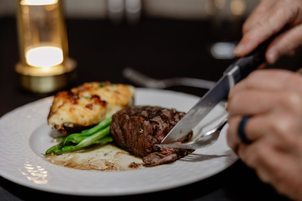 Guest cutting into a steak dinner at Cellar & Flame Steakhouse in Traverse City