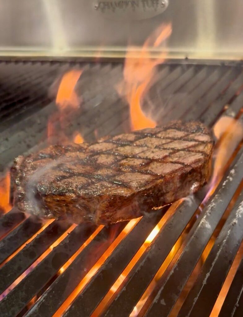 Wood-fired steak cooking over flame at Cellar & Flame Steakhouse in Traverse City